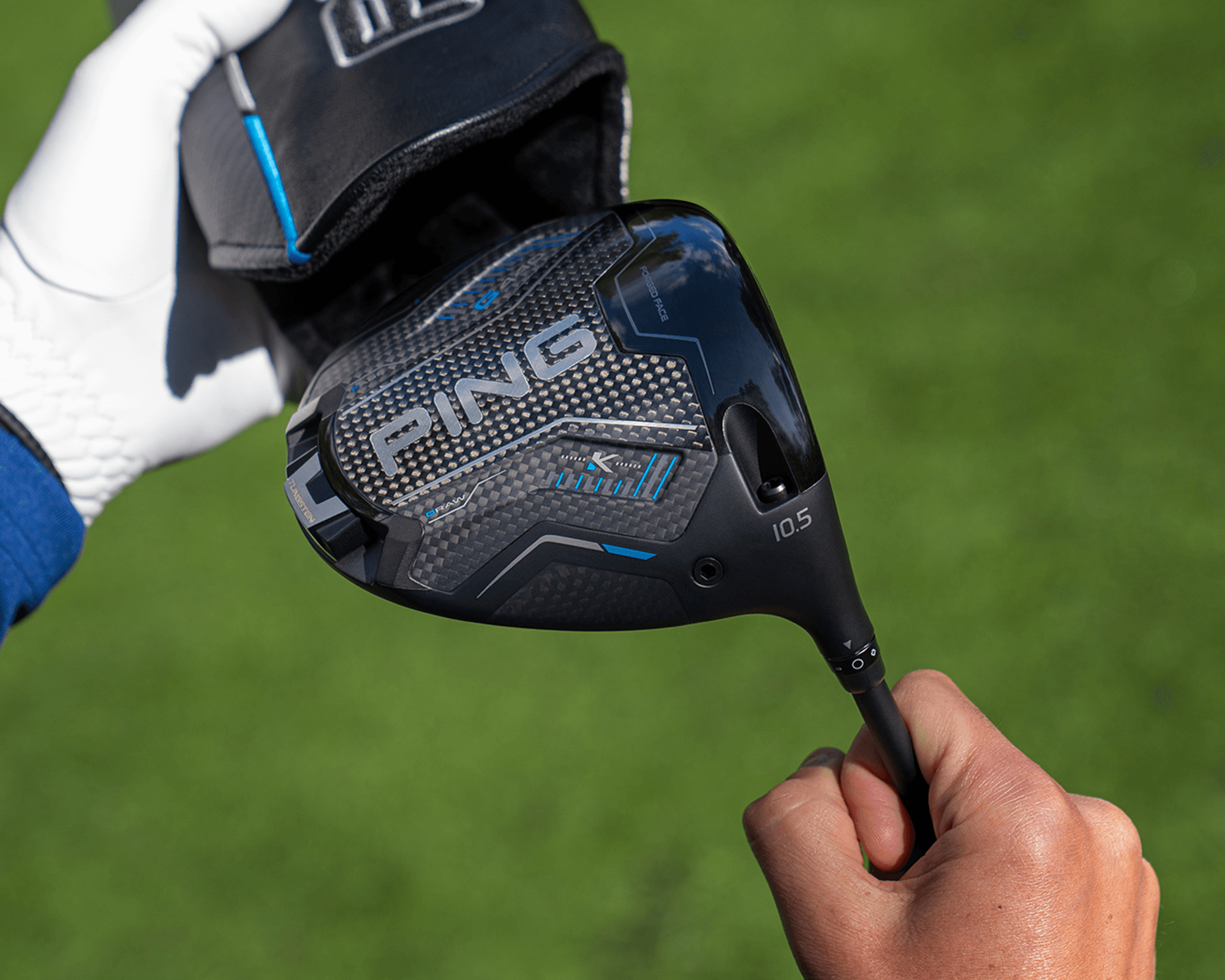 A golfer holding a PING driver while removing it from a headcover on a golf course.